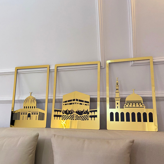 Three gold-framed pictures of architectural landmarks on a beige sofa against a white wall.
