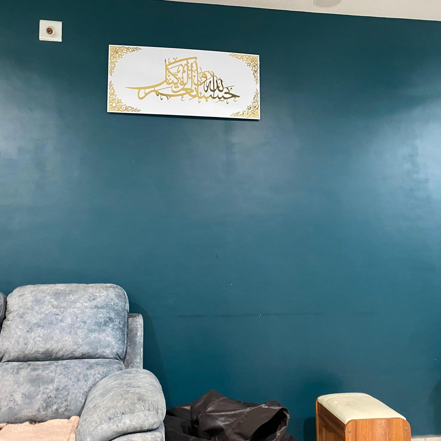 Gray sofa against a teal wall with a decorative plaque featuring Arabic calligraphy.