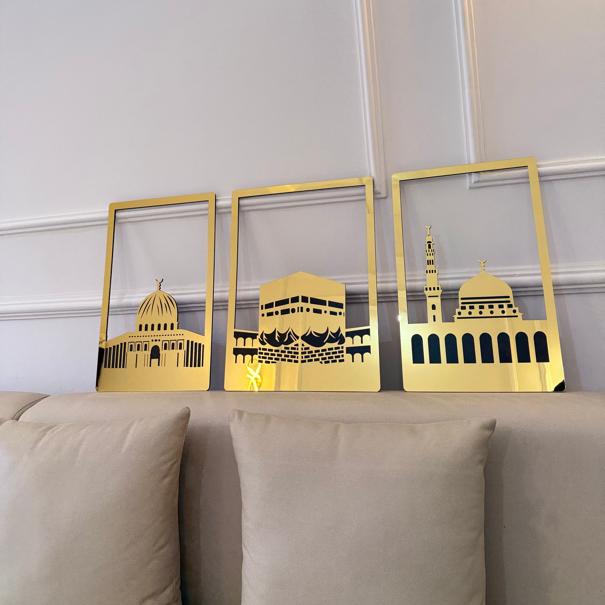 Three gold-framed artworks of architectural designs on a wall above a beige sofa.