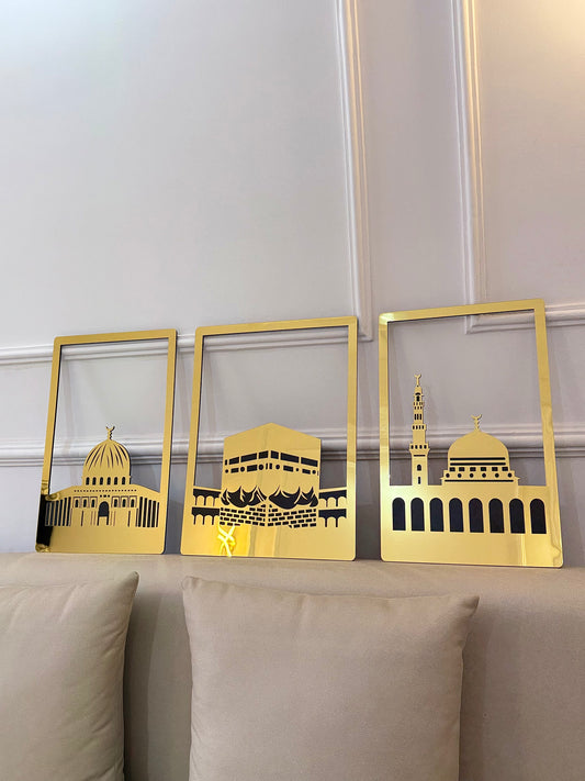 Three gold-framed pictures of architectural landmarks on a beige sofa against a white wall.