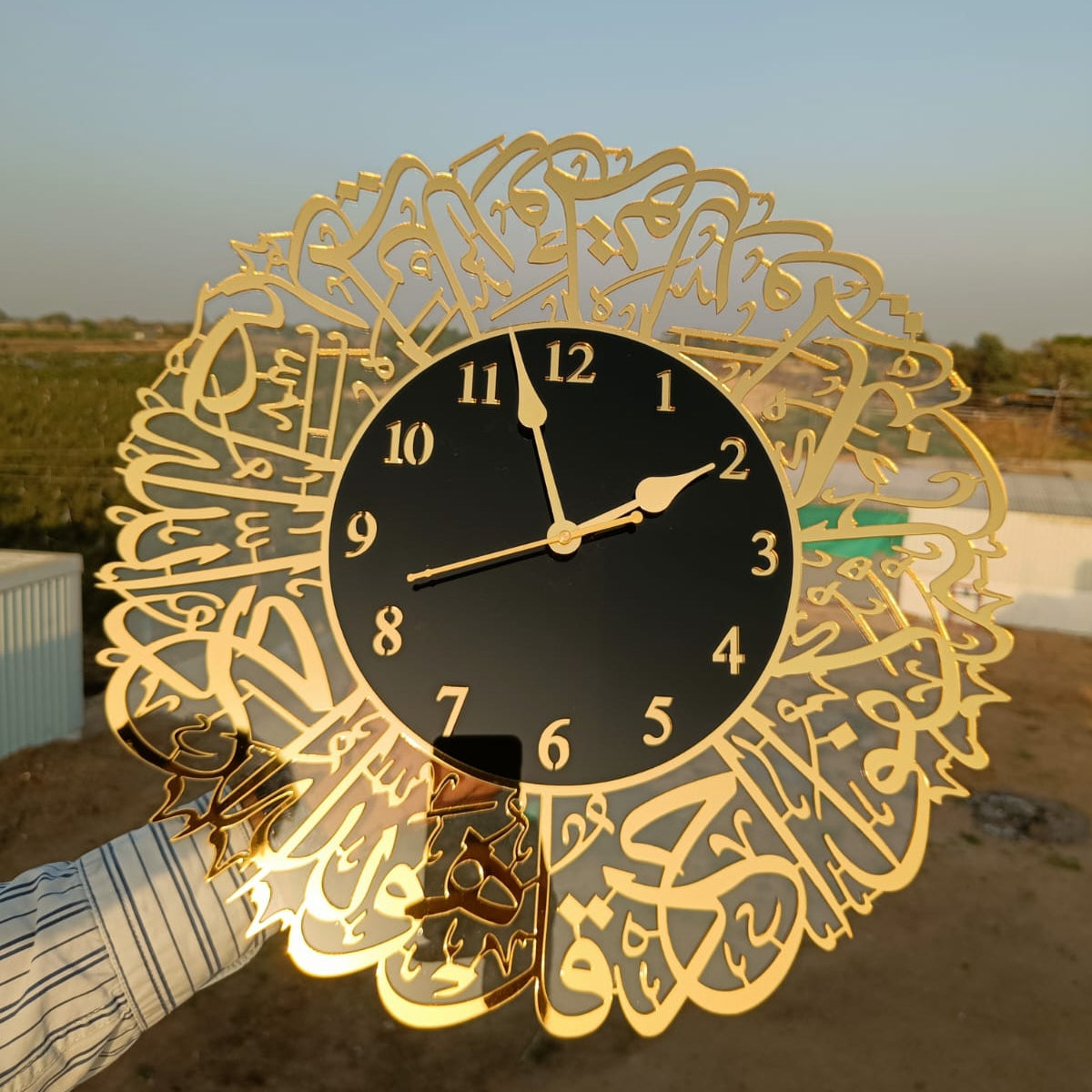 Decorative wall clock with gold intricate design and black face outdoors.
