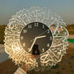 Decorative wall clock with Arabic calligraphy held by a person against a scenic background.
